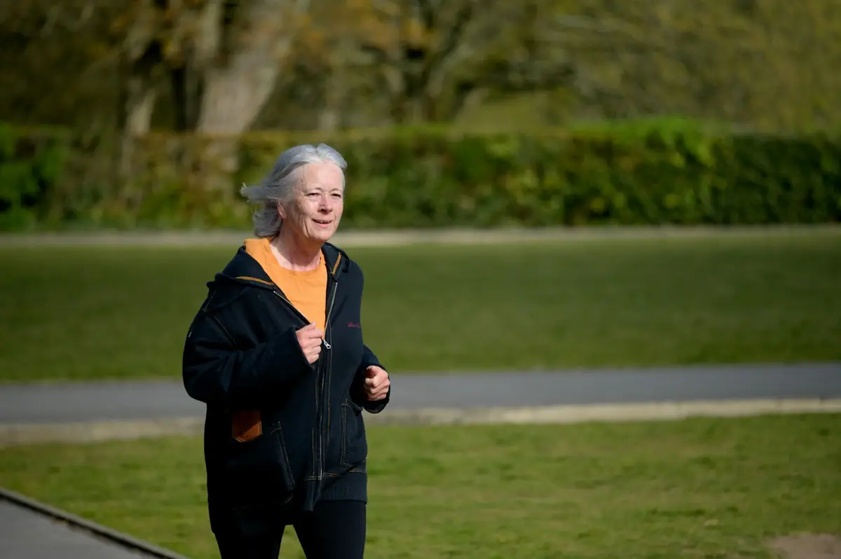 Ältere Frau mit grauen Haaren joggt lächelnd durch einen Park