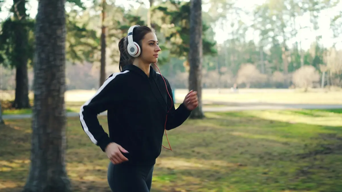 Junge Frau joggt mit Kopfhörern durch einen Park